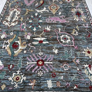 May include: A rectangular area rug featuring a dark blue and brown horizontal striped background with a multi-colored floral and botanical pattern. The design includes various stylized flowers, leaves, and geometric shapes in pink, red, white, and teal, finished with a decorative floral border.
