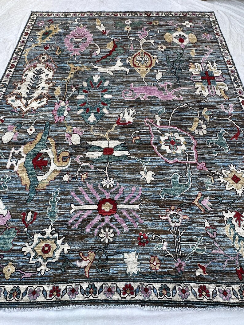 May include: A rectangular area rug featuring a dark blue and brown horizontal striped background with a multi-colored floral and botanical pattern. The design includes various stylized flowers, leaves, and geometric shapes in pink, red, white, and teal, finished with a decorative floral border.