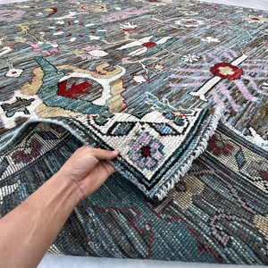 May include: A large area rug featuring a dark brown base with intricate floral and geometric patterns in shades of blue, red, pink, and cream. The rug has a visible pile texture and a fringed edge, with a corner folded over to reveal the underside.