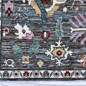 May include: A rectangular area rug featuring a complex floral pattern with a blue and brown striated background. The design includes stylized flowers in shades of pink, red, white, and teal, framed by a decorative border with repeating floral motifs.