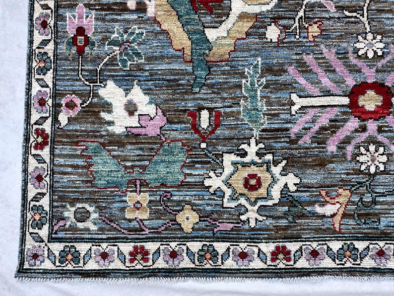 May include: A rectangular area rug featuring a complex floral pattern with a blue and brown striated background. The design includes stylized flowers in shades of pink, red, white, and teal, framed by a decorative border with repeating floral motifs.