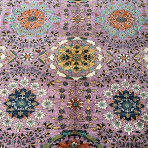 May include: A woven rug featuring a lavender purple background with a repeating pattern of intricate floral medallions in shades of teal, orange, mustard yellow, and dark blue, accented by small white and green botanical motifs throughout the design.