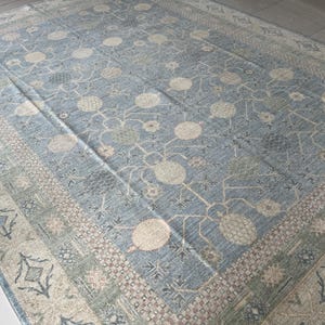 May include: A rectangular area rug featuring a dusty blue field with a repeating pattern of cream-colored circular motifs and thin, branching lines. The border displays a geometric design in shades of beige, sage green, and blue with diamond shapes.