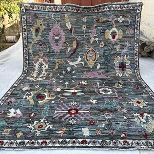 May include: A large rectangular area rug with a dark blue base featuring a complex, multi-colored floral and botanical pattern. The design includes various stylized blossoms, vines, and geometric motifs in shades of pink, cream, red, and teal.