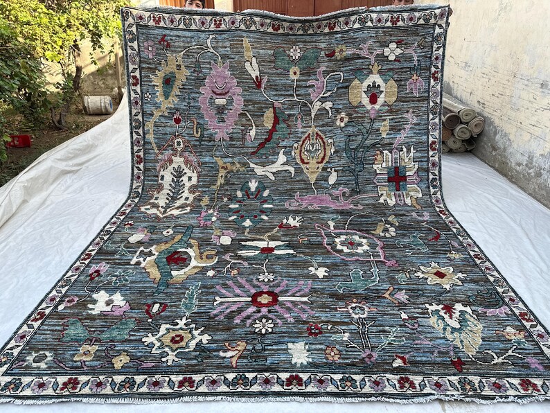 May include: A large rectangular area rug with a dark blue base featuring a complex, multi-colored floral and botanical pattern. The design includes various stylized blossoms, vines, and geometric motifs in shades of pink, cream, red, and teal.