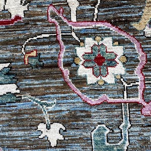 May include: A woven rug featuring a complex pattern with a dark brown and blue textured background. The design includes stylized floral motifs in white, teal, and red, outlined with thin pink lines, creating a detailed and layered visual effect.