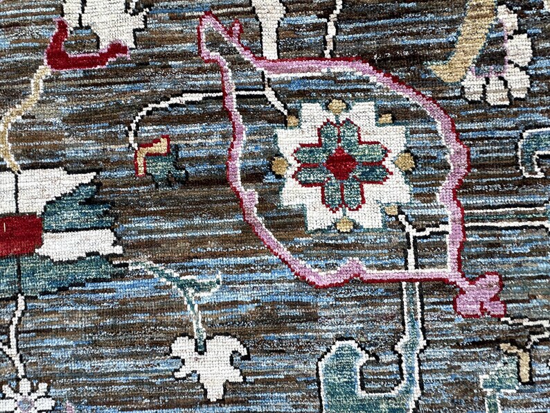May include: A woven rug featuring a complex pattern with a dark brown and blue textured background. The design includes stylized floral motifs in white, teal, and red, outlined with thin pink lines, creating a detailed and layered visual effect.