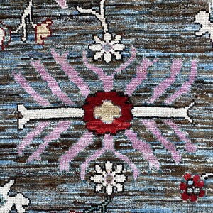 May include: A woven rug featuring a dark brown and blue textured background with a central floral motif in red, white, and light purple. The design includes repeating white flower shapes and intricate botanical patterns across the surface.