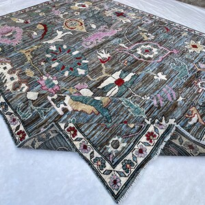 May include: A rectangular area rug featuring a dark blue and brown striped background with an intricate floral pattern in shades of pink, red, white, and teal. The rug has a decorative border with small flower motifs and a short white fringe edge.