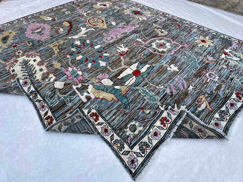 May include: A rectangular area rug featuring a dark blue and brown striped background with an intricate floral pattern in shades of pink, red, white, and teal. The rug has a decorative border with small flower motifs and a short white fringe edge.