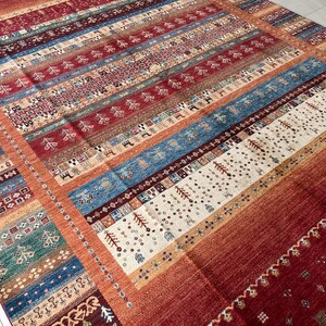 May include: A rectangular area rug featuring a vibrant, multi-colored striped pattern. The design incorporates horizontal bands of deep red, bright blue, cream, and teal, decorated with small, repeating geometric motifs, tree shapes, and animal figures.