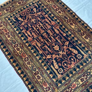 May include: A rectangular area rug featuring a dark navy blue field with intricate geometric and floral patterns in shades of tan, rust red, and cream. The rug has a wide, multi-layered border with repeating motifs and a short fringe edge.