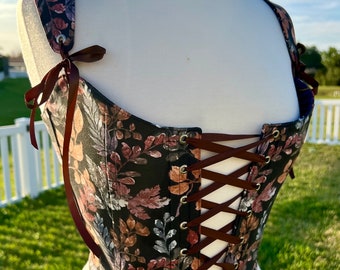 May include: A black corset with a floral print featuring brown, pink, and blue leaves. The corset has brown ribbon lacing in the back.
