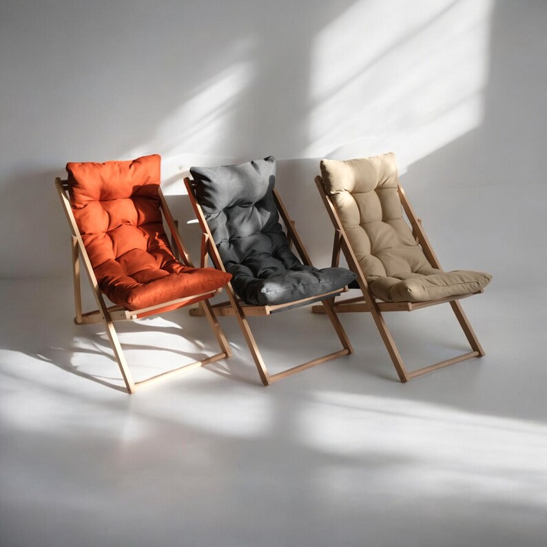 May include: Three wooden folding chairs with different colored cushions. The chair on the left has an orange cushion, the middle chair has a gray cushion, and the chair on the right has a beige cushion.