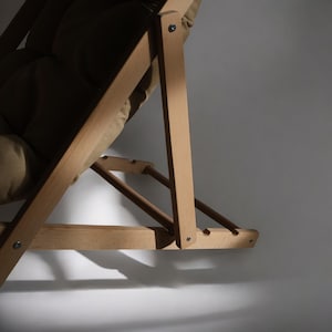 May include: A wooden folding chair with a brown fabric seat and back. The chair is made of natural wood and has a simple design.