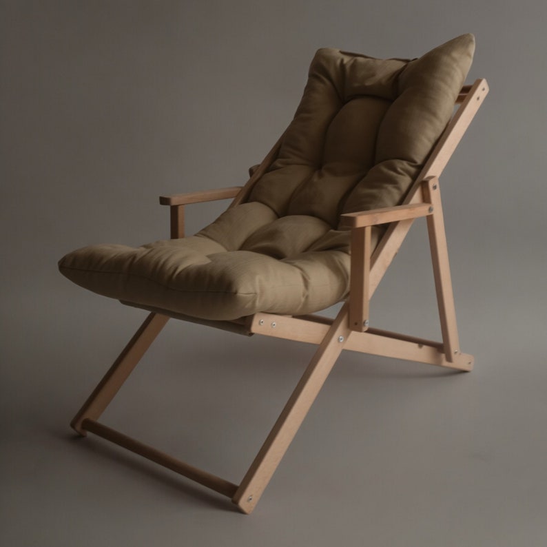 May include: A light brown wooden folding chair with a beige fabric cushion. The chair has a simple design with a slightly reclined back and a footrest.