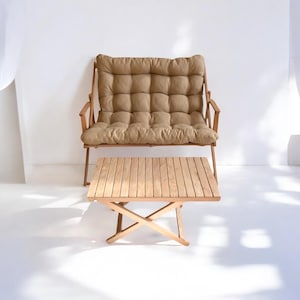 May include: A light brown cushioned wooden bench with a matching wooden folding table in front of it. The bench and table are on a white surface.