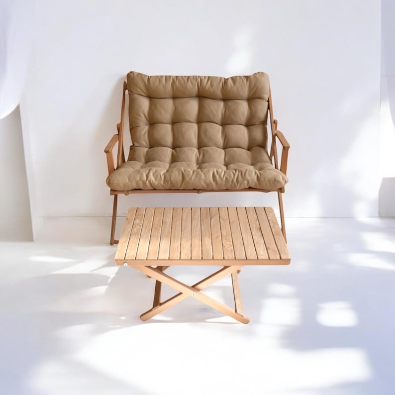 May include: A light brown cushioned wooden bench with a matching wooden folding table in front of it. The bench and table are on a white surface.
