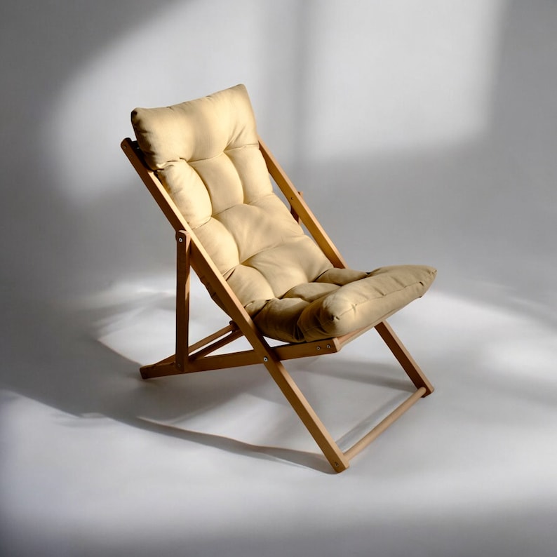 May include: A light brown wooden folding chair with a beige padded cushion. The chair is reclined and has a simple design.