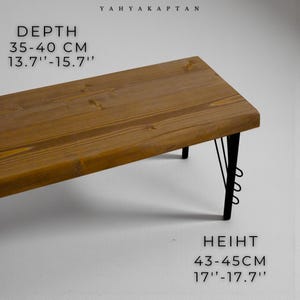 K&ouml;nnte beinhalten: Eine Holzbank mit nat&uuml;rlicher brauner Oberfl&auml;che und schwarzen Metallbeinen. Der Text YAHYA KAPTAN ist sichtbar. Die auf dem Bild angegebenen Ma&szlig;e betragen 35-40 cm Tiefe und 43-45 cm H&ouml;he.
