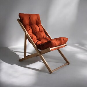 May include: A wooden folding chair with a rust-colored padded seat and back.
