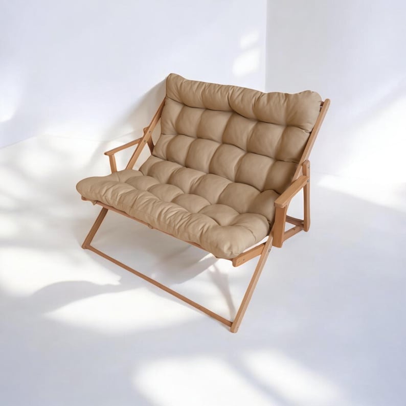 May include: A light brown wooden folding loveseat with a beige padded cushion. The cushion has a tufted design with multiple square buttons.