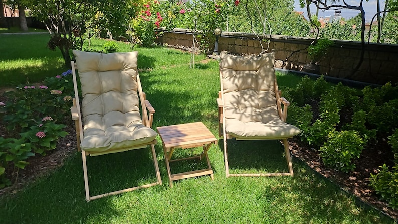 May include: Two wooden folding chairs with beige cushions and a small wooden folding table in a grassy garden setting.