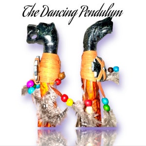 May include: Two black and green stone animal head pendulums with orange, brown, and multi-colored beads and feathers. The text "The Dancing Pendulum" is at the top of the image.