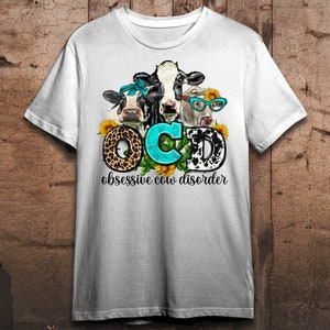 May include: White t-shirt featuring a graphic of three cows with sunflowers and the text "OCD obsessive cow disorder." The letters "OCD" are styled with a leopard print, turquoise, and a black and white cow pattern.