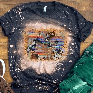 May include: A black t-shirt with a bleach-splattered design featuring a colorful abstract pattern with animal print accents.