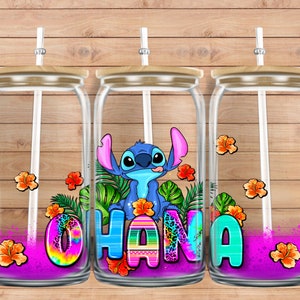 May include: Three clear glass tumblers with lids and straws. Each tumbler features a pink, purple and blue ombre design with a cartoon Stitch character and the word "Ohana" in colourful letters. The tumblers are on a wood background.