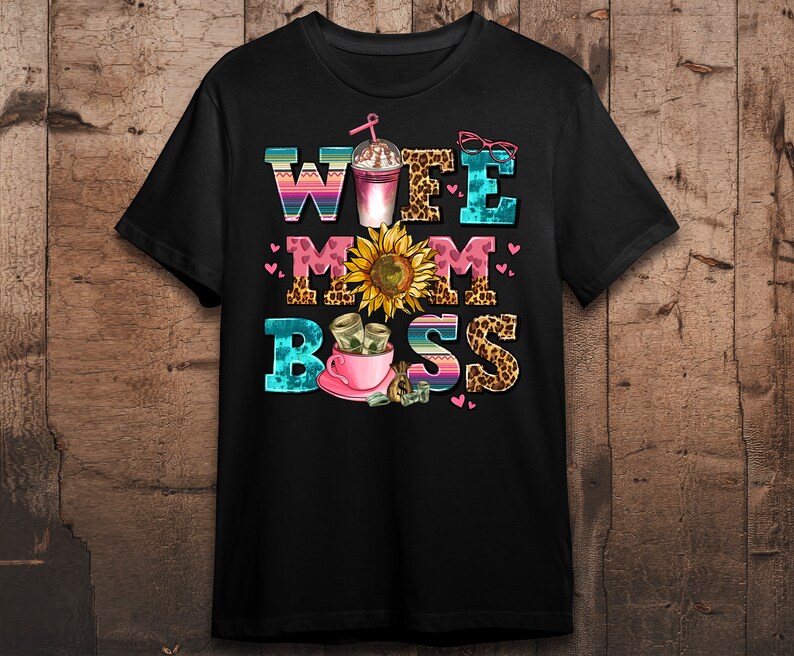 Puede incluir: Camiseta negra con un dise&ntilde;o gr&aacute;fico colorido que dice "Wife Mom Boss" con un girasol, una taza de caf&eacute; y dinero.