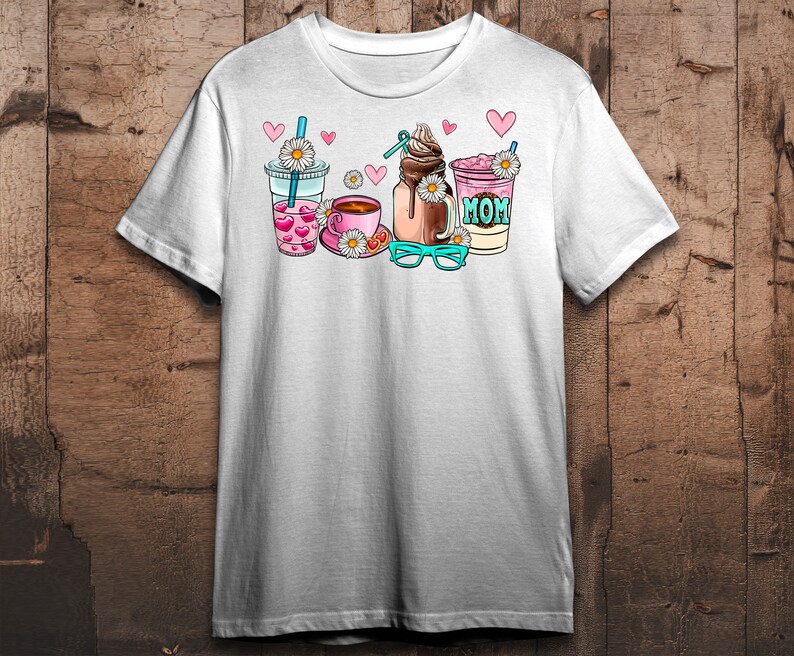 May include: White t-shirt with a graphic of four drinks: a pink iced coffee, a brown iced coffee, a pink milkshake with the word "MOM" on it, and a pink iced tea. The graphic also includes hearts, daisies, and a pair of blue glasses.