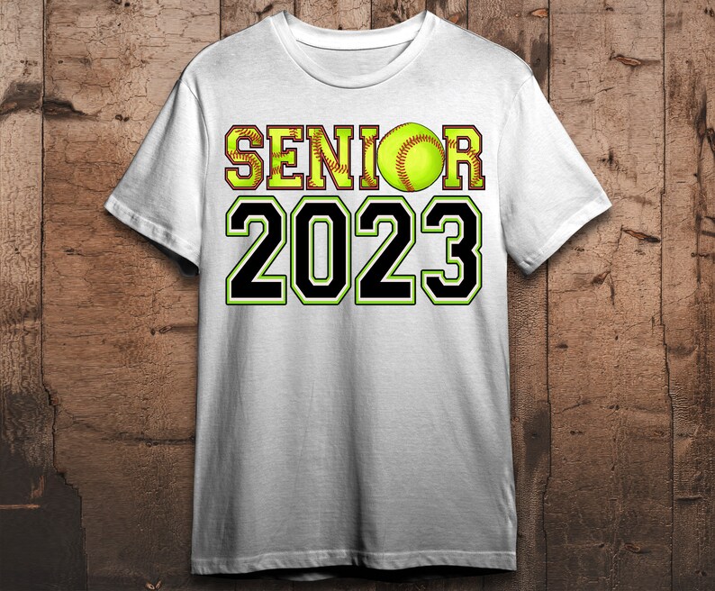 Peut inclure: T-shirt blanc avec un texte noir qui dit "Senior 2023" et une balle de softball jaune avec des coutures rouges.