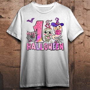 K&ouml;nnte beinhalten: Wei&szlig;es T-Shirt mit einer pinkfarbenen und wei&szlig;en Grafik einer Mumie und eines Geistes. Die Grafik lautet "My 1st Halloween".