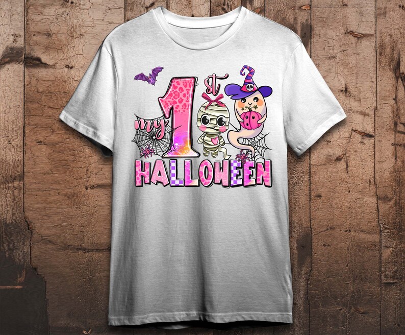 K&ouml;nnte beinhalten: Wei&szlig;es T-Shirt mit einer pinkfarbenen und wei&szlig;en Grafik einer Mumie und eines Geistes. Die Grafik lautet "My 1st Halloween".