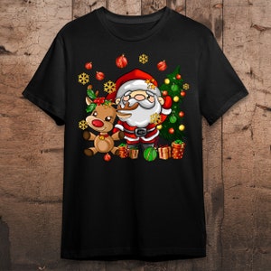 Pode incluir: Uma camiseta preta com uma imagem de desenho animado do Papai Noel e uma rena. O Papai Noel est&aacute; vestindo um terno vermelho com detalhes brancos e uma barba branca. A rena &eacute; marrom com o nariz vermelho. Ambos est&atilde;o em p&eacute; na frente de uma &aacute;rvore de Natal verde com enfeites vermelhos e dourados.