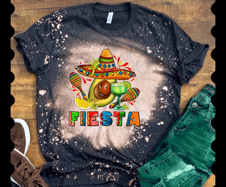 May include: A black t-shirt with a bleach-splattered design featuring a cartoon avocado wearing a sombrero and holding a margarita. The text "FIESTA" is written in colorful letters below the avocado.