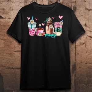 May include: Black t-shirt with a graphic of four drinks: a coffee cup, a milkshake, a smoothie, and a iced coffee. The graphic includes hearts, daisies, and the word "MOM".