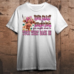 May include: White t-shirt with a cartoon Highland cow wearing a pink bow. The text reads "Your crazy is showing you might want to tuck that back in."