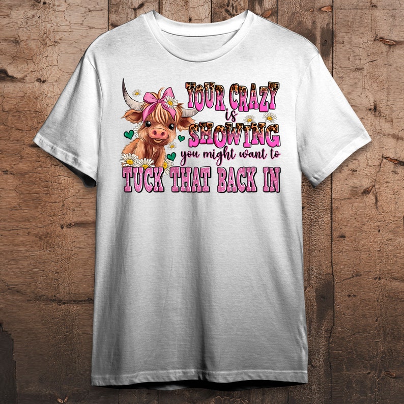 May include: White t-shirt with a cartoon Highland cow wearing a pink bow. The text reads "Your crazy is showing you might want to tuck that back in."