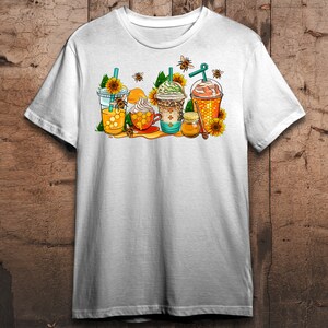 May include: White t-shirt with a graphic of four iced coffee drinks decorated with honeycombs, sunflowers, and bees. The text "Honeycomb" is printed on the shirt.