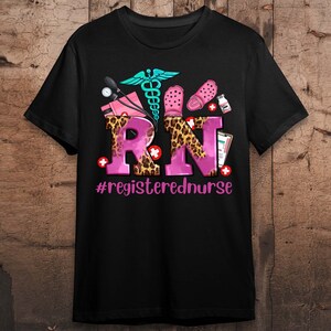 K&ouml;nnte beinhalten: Schwarzes T-Shirt mit einem rosafarbenen und leopardenfarbenen "RN"-Design. Das Design beinhaltet ein Stethoskop, eine medizinische Tasche und ein Paar rosa Clogs. Der Text "#registerednurse" befindet sich unter dem Design.