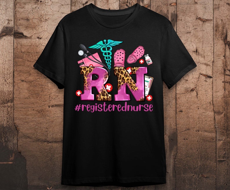 K&ouml;nnte beinhalten: Schwarzes T-Shirt mit einem rosafarbenen und leopardenfarbenen "RN"-Design. Das Design beinhaltet ein Stethoskop, eine medizinische Tasche und ein Paar rosa Clogs. Der Text "#registerednurse" befindet sich unter dem Design.