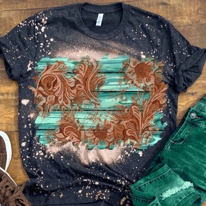 May include: A black t-shirt with a bleach-splattered design featuring a brown floral pattern on a turquoise and white striped background.