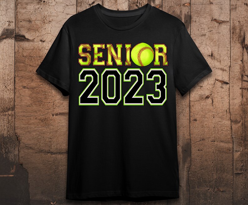 Peut inclure: T-shirt noir avec du texte blanc qui dit "Senior 2023" et un ballon de softball jaune au milieu du texte.