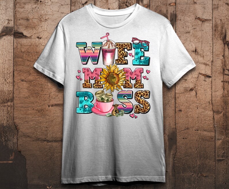 Puede incluir: Camiseta blanca con un dise&ntilde;o gr&aacute;fico colorido que dice "Wife Mom Boss" con un girasol, una taza de caf&eacute; y dinero.