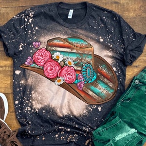 May include: A black t-shirt with a bleached design of a turquoise and brown cowboy hat with pink and white flowers.