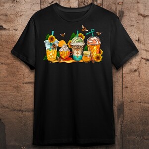 May include: Black t-shirt with a graphic of four iced coffee drinks decorated with honeycombs, bees, and sunflowers.