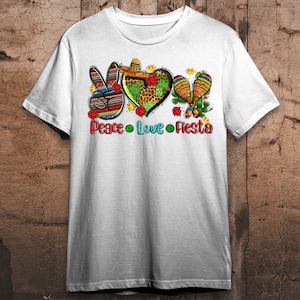Puede incluir: Camiseta blanca con un gr&aacute;fico de signo de paz, coraz&oacute;n y maracas. El gr&aacute;fico est&aacute; en un estilo mexicano colorido con rojo, amarillo, verde, azul y negro. El texto "Peace Love Fiesta" est&aacute; debajo del gr&aacute;fico.